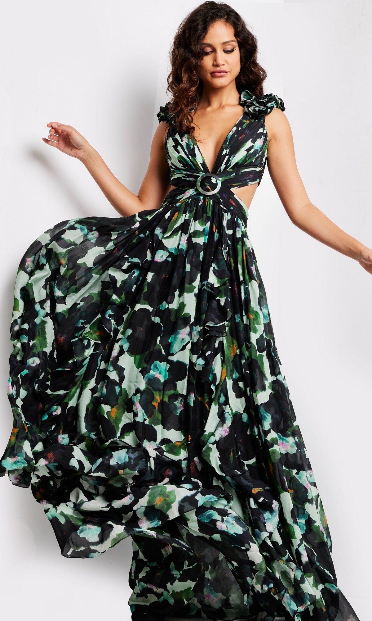 A woman models the Long Prom Dress 39420 by Jovani—a sleeveless, deep V-neck formal gown with cut-out sides, open back, and a black base featuring green and blue floral patterns—standing against a plain white background.